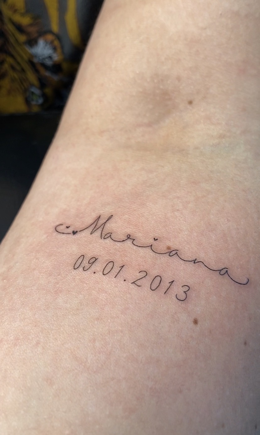Tatuagem de nome e data em traço delicado